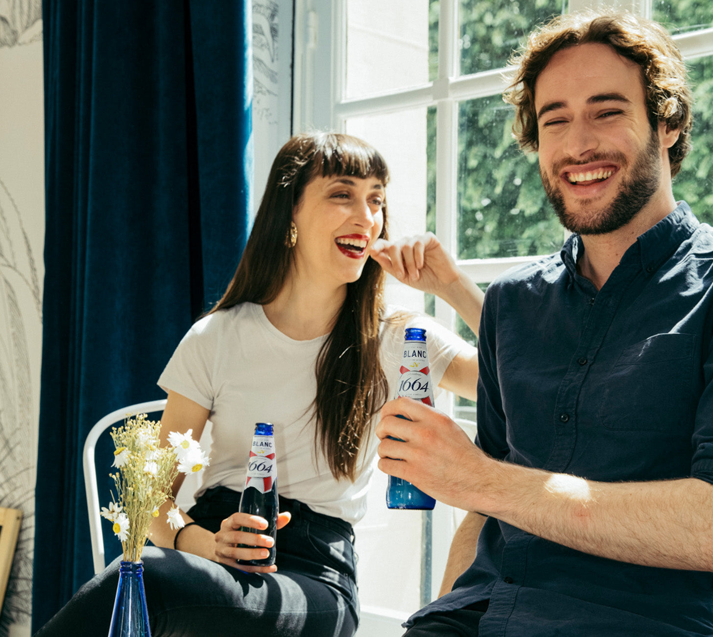 DE: Zwei Personen geniessen gemeinsam Kronenbourg 1664 Blanc in Glasflaschen, lachend am Fenster im Sonnenlicht.

FR: Deux personnes dégustent ensemble un Kronenbourg 1664 Blanc en bouteille, riant près de la fenêtre sous la lumière du soleil.

IT: Due persone gustano insieme una Kronenbourg 1664 Blanc in bottiglia, sorridendo vicino alla finestra alla luce del sole.