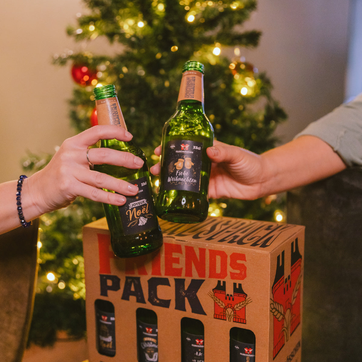 DE: Stimmungsbild mit Feldschloesschen Friends Pack Weihnachten – zwei Personen stossen mit festlich gestalteten Bierflaschen an, Weihnachtsbaum mit Lichtern im Hintergrund.
FR: Photo d’ambiance avec Feldschloesschen Friends Pack Noël – deux personnes trinquent avec des bouteilles festives, sapin de Noël illuminé en arrière-plan.
IT: Immagine d’atmosfera con Feldschloesschen Friends Pack Natale – due persone brindano con bottiglie festive, albero di Natale illuminato sullo sfondo.