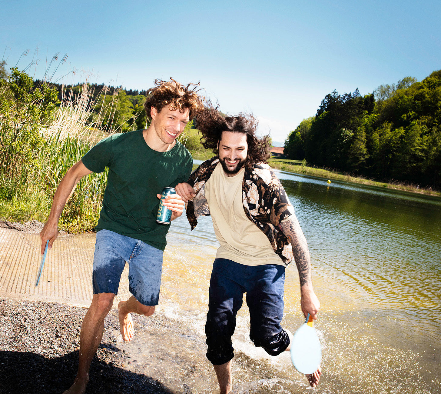DE: Zwei Männer am See mit USZIT Lager Dose, Sommerstimmung in der Natur.
FR: Deux hommes au bord d’un lac avec une cannette USZIT, ambiance estivale.
IT: Due uomini al lago con lattina USZIT, atmosfera estiva nella natura.