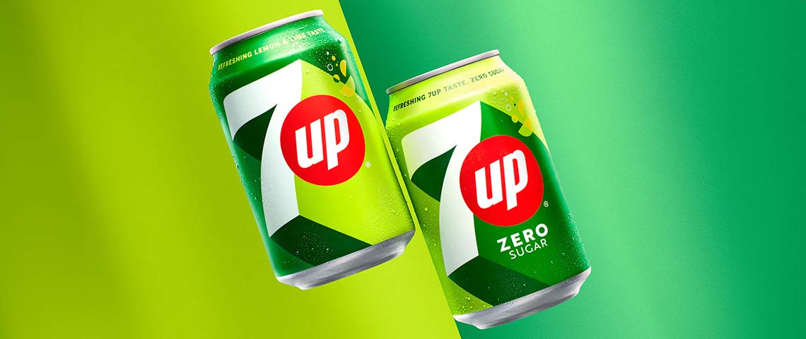 DE: 7UP Original und Zero Sugar Dosen nebeneinander auf grünem Hintergrund FR: Canettes 7UP Original et Zero Sugar côte à côte sur fond vert IT: Lattine 7UP Original e Zero Sugar affiancate su sfondo verde EN: 7UP Original and Zero Sugar cans side by side on green background