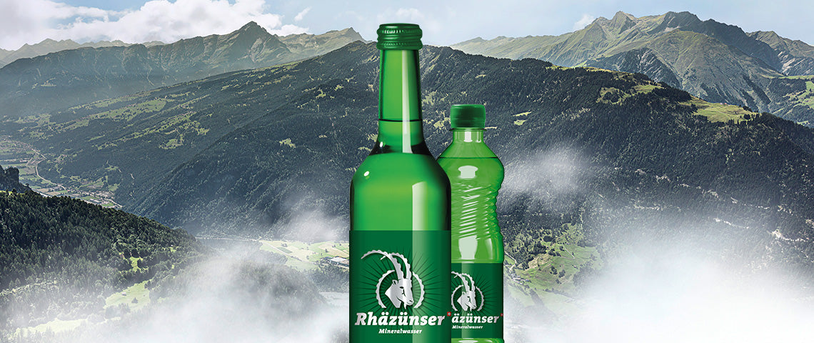 DE: Zwei Rhäzünser Flaschen vor imposantem Bergpanorama der Bündner Berge FR: Deux bouteilles Rhäzünser devant un imposant panorama des Alpes grisonnes IT: Due bottiglie Rhäzünser davanti a imponente panorama alpino grigionese EN: Two Rhäzünser bottles in front of impressive Graubünden mountain panorama
