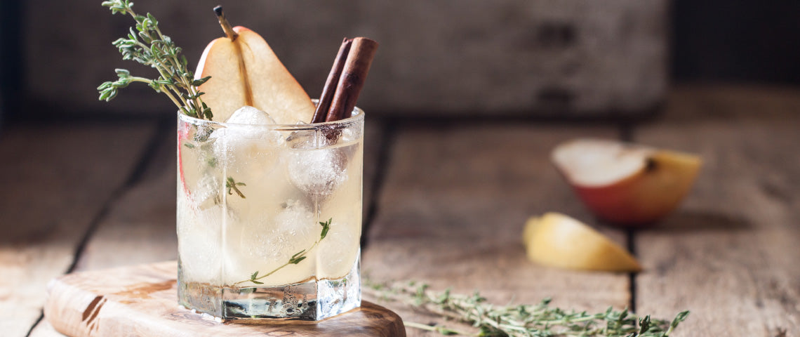 DE: Zwei Cider-Gläser mit Birne, Rosmarin und Eiswürfeln auf dunklem Holztisch FR: Deux verres de cidre avec poire, romarin et glaçons sur table en bois sombre IT: Due bicchieri di sidro con pera, rosmarino e cubetti di ghiaccio su tavolo scuro EN: Two cider glasses with pear, rosemary and ice cubes on dark wooden table