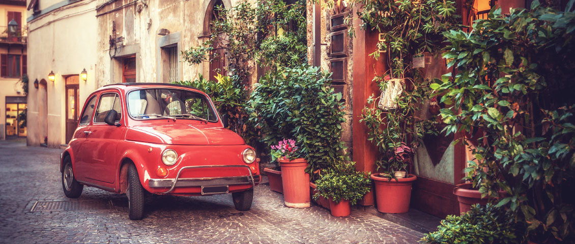 DE: Roter Fiat 500 vor farbenfroher Hausfassade mit Blumentöpfen in Italien FR: Fiat 500 rouge devant façade colorée avec pots de fleurs en Italie IT: Fiat 500 rossa davanti a facciata colorata con vasi di fiori in Italia EN: Red Fiat 500 in front of colourful house facade with flower pots in Italy