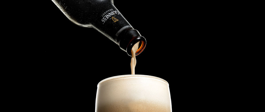 DE: Guinness wird aus dunkler Flasche in Glas eingegossen mit cremigem Schaum FR: Guinness versé d'une bouteille sombre dans un verre avec mousse crémeuse IT: Guinness versato da bottiglia scura in bicchiere con schiuma cremosa EN: Guinness being poured from dark bottle into glass with creamy foam