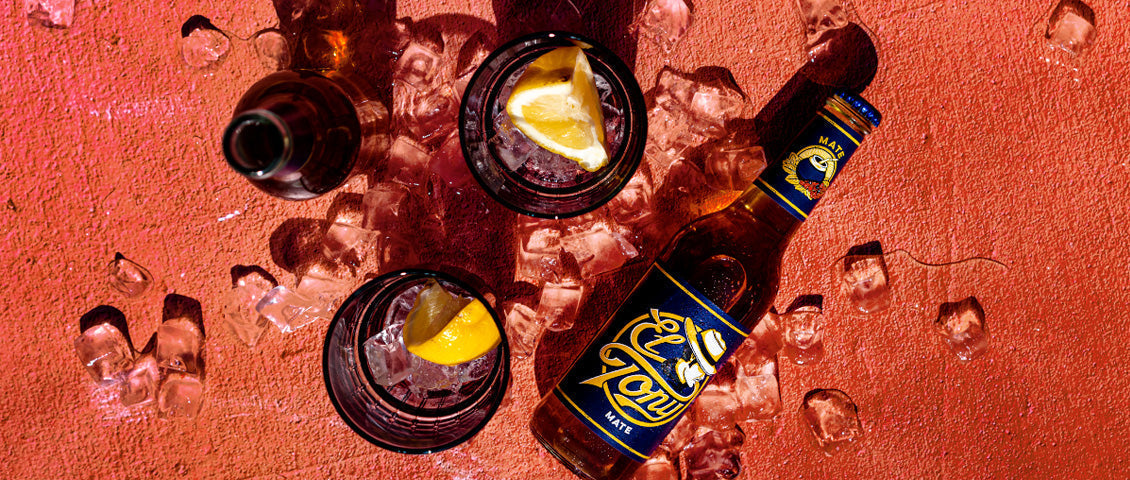 DE: El Tony Mate Dosen auf Eis mit Orangenscheiben von oben fotografiert FR: Canettes El Tony Mate sur glace avec tranches d'orange photographiées de dessus IT: Lattine El Tony Mate su ghiaccio con fette d'arancia fotografate dall'alto EN: El Tony Mate cans on ice with orange slices photographed from above