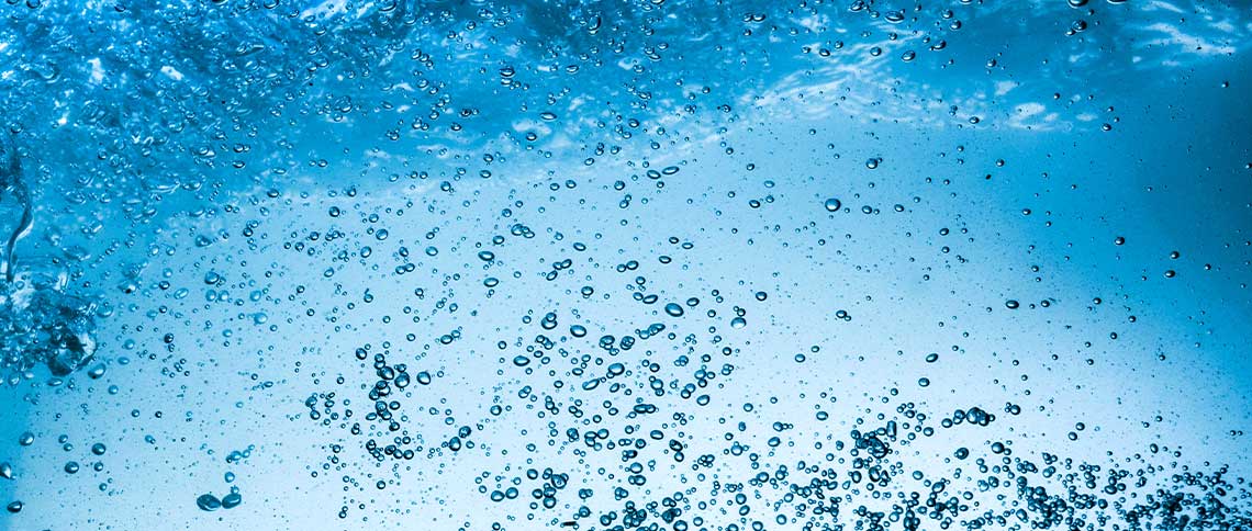 DE: Sprudelndes Mineralwasser mit Blasen in Nahaufnahme von oben FR: Eau minérale pétillante avec bulles en gros plan vue de dessus IT: Acqua minerale frizzante con bolle in primo piano vista dall'alto EN: Sparkling mineral water with bubbles in close-up from above