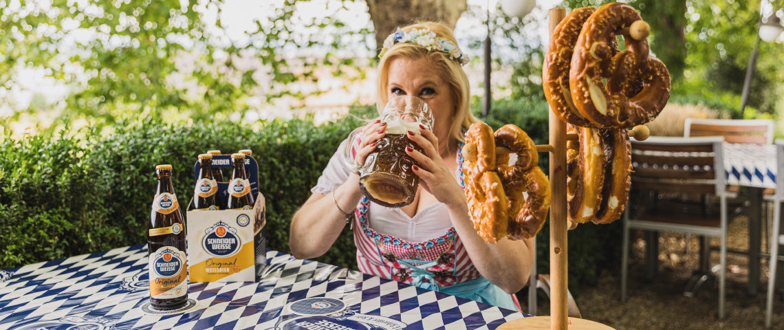 DE: Frau in Tracht trinkt Schneider Weisse Original mit Brezeln im Hintergrund FR: Femme en costume traditionnel buvant Schneider Weisse Original avec bretzels IT: Donna in costume tradizionale beve Schneider Weisse Original con bretzel EN: Woman in traditional costume drinking Schneider Weisse Original with pretzels