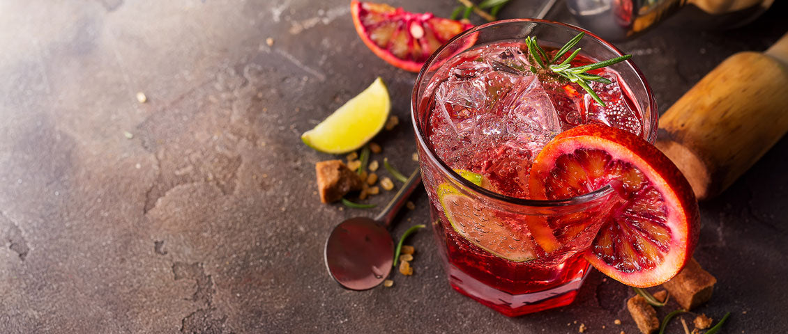 DE: Roter Sanbitter Mocktail mit Granatapfel, Limette und Rosmarin auf dunklem Untergrund FR: Mocktail Sanbitter rouge avec grenade, citron vert et romarin sur fond sombre IT: Mocktail Sanbitter rosso con melograno, lime e rosmarino su sfondo scuro EN: Red Sanbitter mocktail with pomegranate, lime and rosemary on dark background