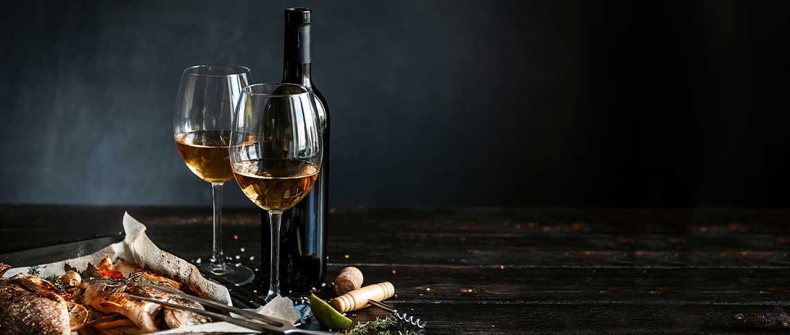 DE: Zwei Weingläser und Weinflasche auf dunklem Holztisch in stimmungsvollem Licht FR: Deux verres de vin et bouteille sur table en bois sombre dans lumière tamisée IT: Due bicchieri di vino e bottiglia su tavolo scuro in legno con luce soffusa EN: Two wine glasses and bottle on dark wooden table in atmospheric light