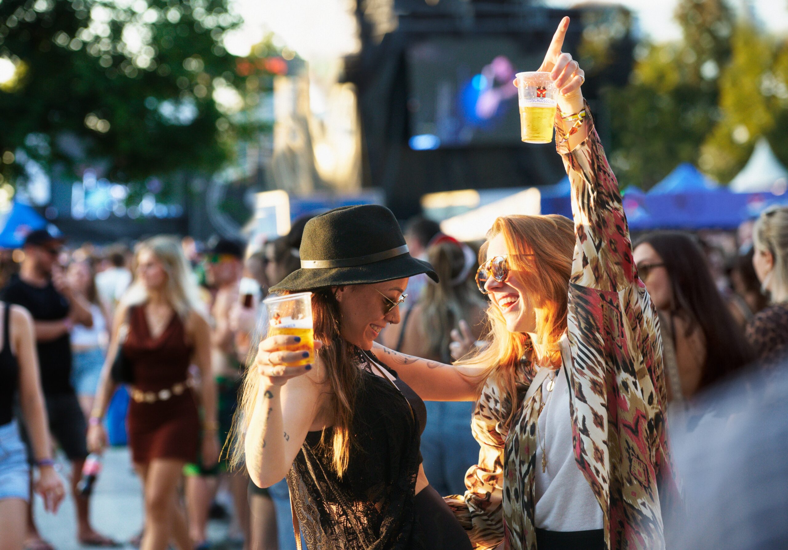 DE: Zwei Frauen tanzen am Festival vor der Bühne mit je einem Feldschlösschen Bier in der Hand.; FR: Deux femmes dansent devant la scène d'un festival, chacune avec une bière Feldschlösschen à la main; IT: Due donne ballano davanti al palco di un festival, ognuna con una birra Feldschlösschen in mano; EN: Two women dancing in front of the stage at a festival, each holding a Feldschlösschen beer in hand