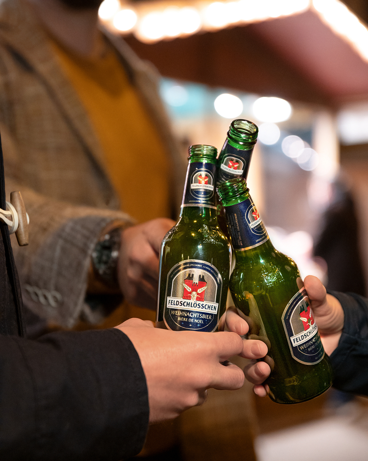 DE: Drei Personen stossen mit dem Feldschlösschen Weihnachtsbier an.; FR: Trois personnes trinquent avec la bière de Noël Feldschlösschen; IT: Tre persone brindano con la birra di Natale Feldschlösschen; EN: Three people toasting with Feldschlösschen Christmas beer